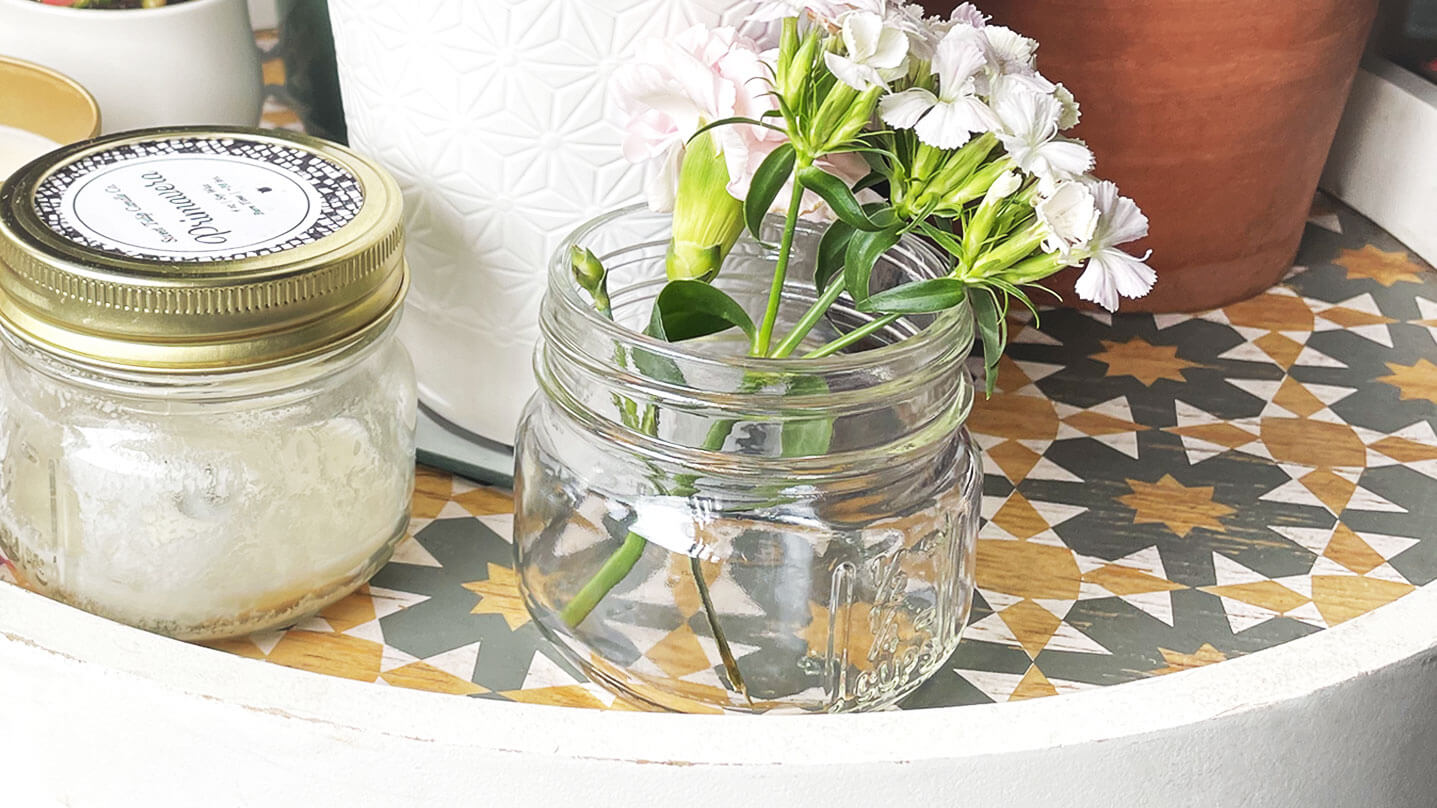 Mini Mason candle jar—refillable, reusable glass. Clean, plant-filled window scene with a white flower for purity. Eco-friendly home decor idea.